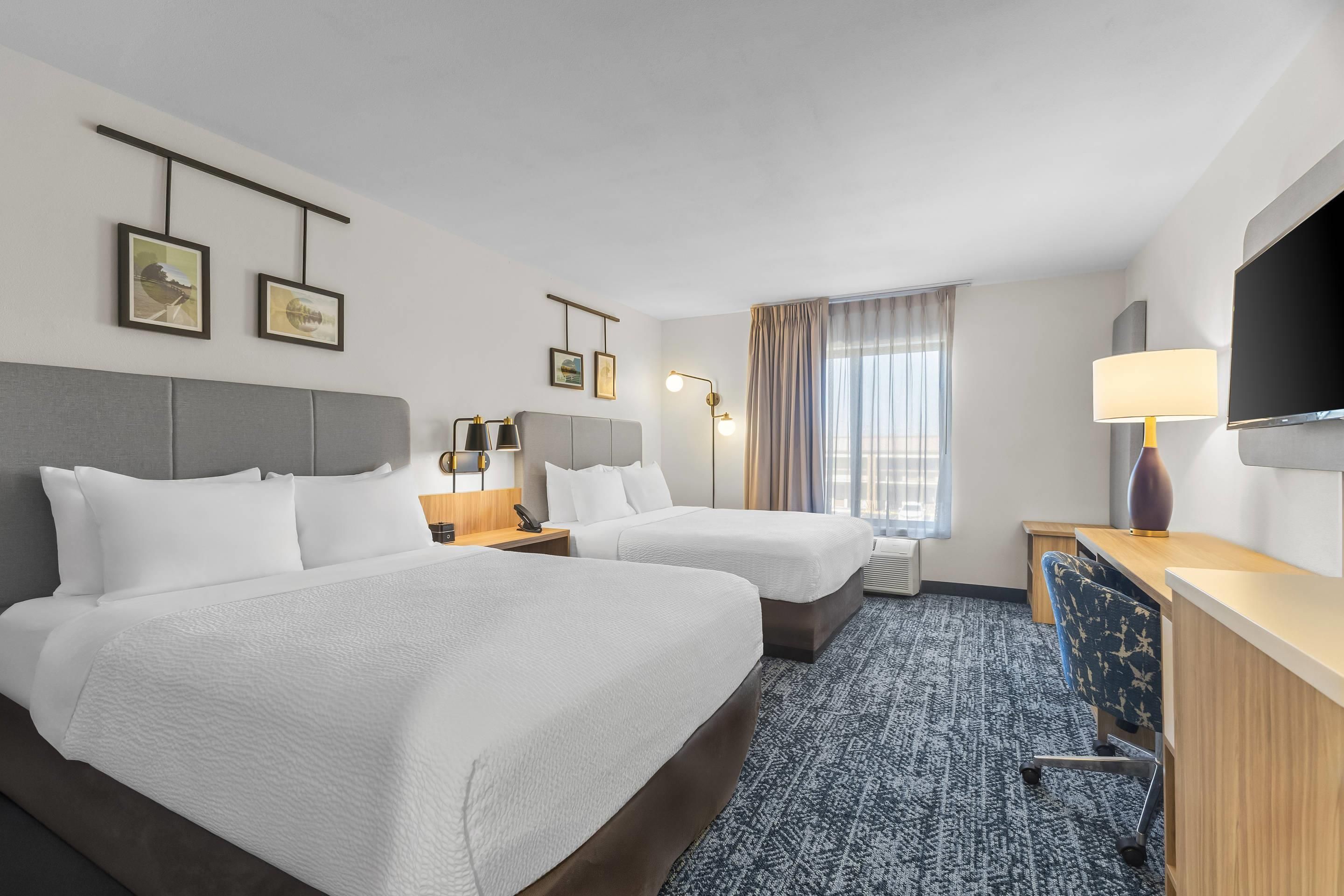 Habitación de hotel con dos camas, un escritorio, una silla, un televisor y una ventana con cortinas.