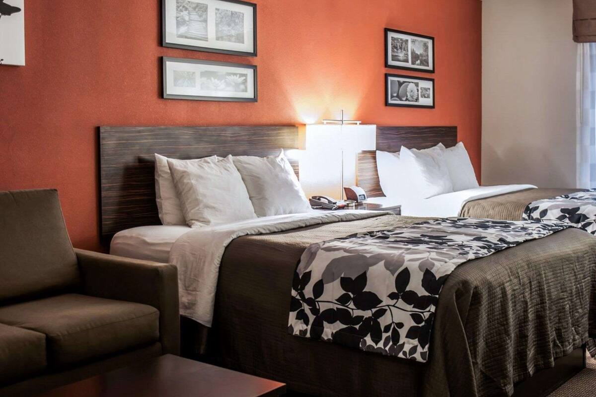 Habitación de hotel con dos camas, un sofá, un escritorio y cuadros en la pared.
