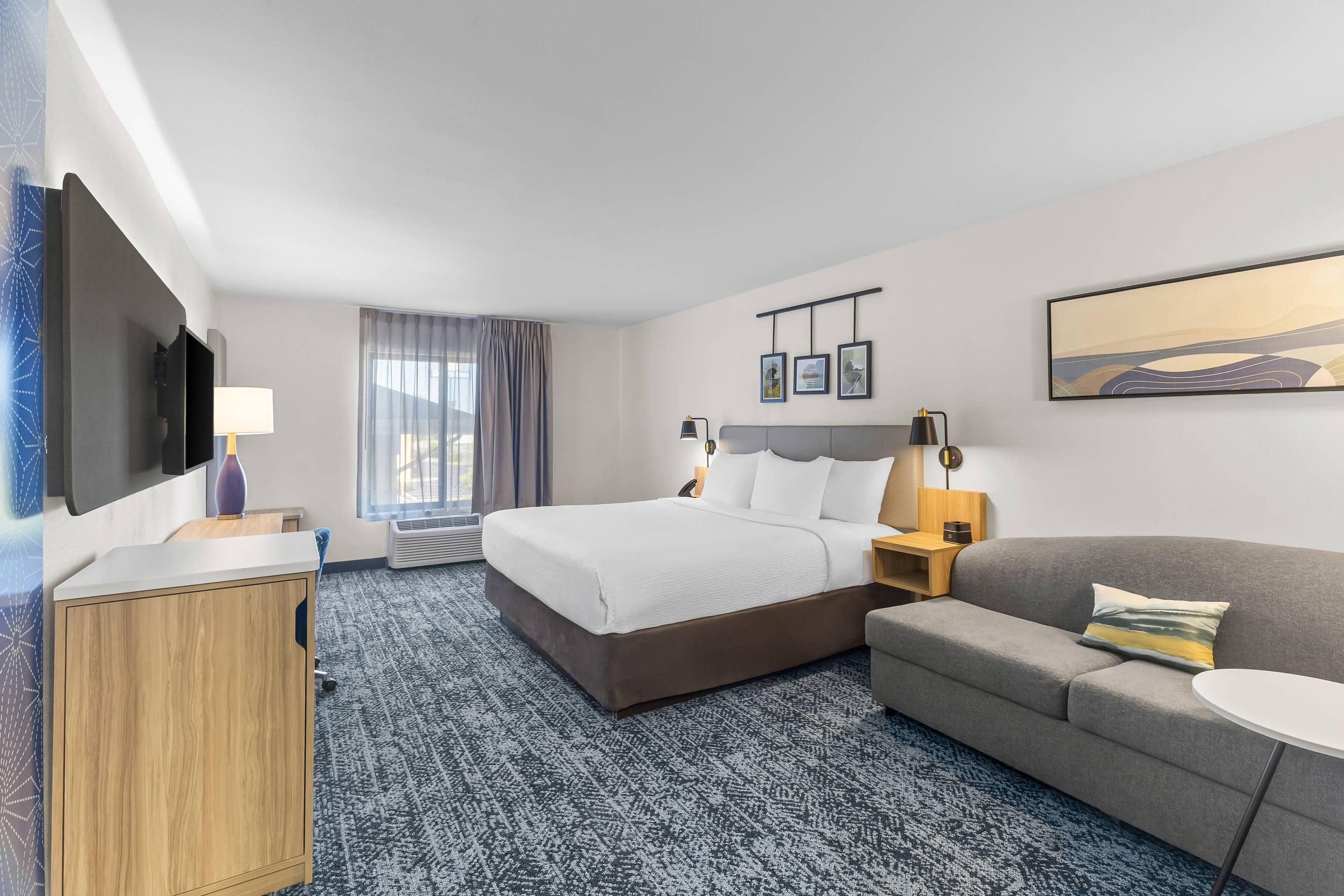 A hotel room with a bed, a sofa, a desk, a TV, and a window with curtains.