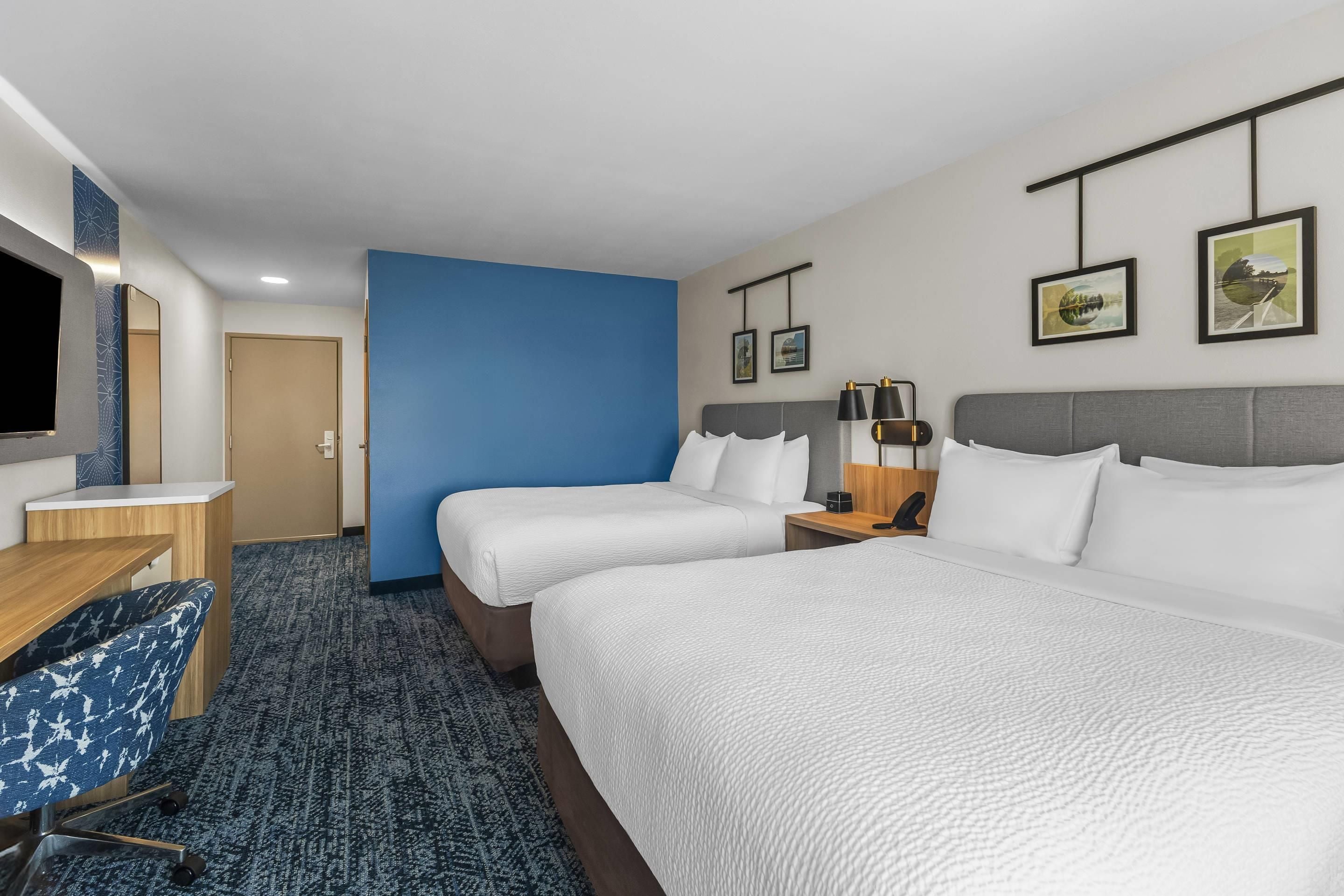 A hotel room with two beds, a desk, a chair, and a TV.