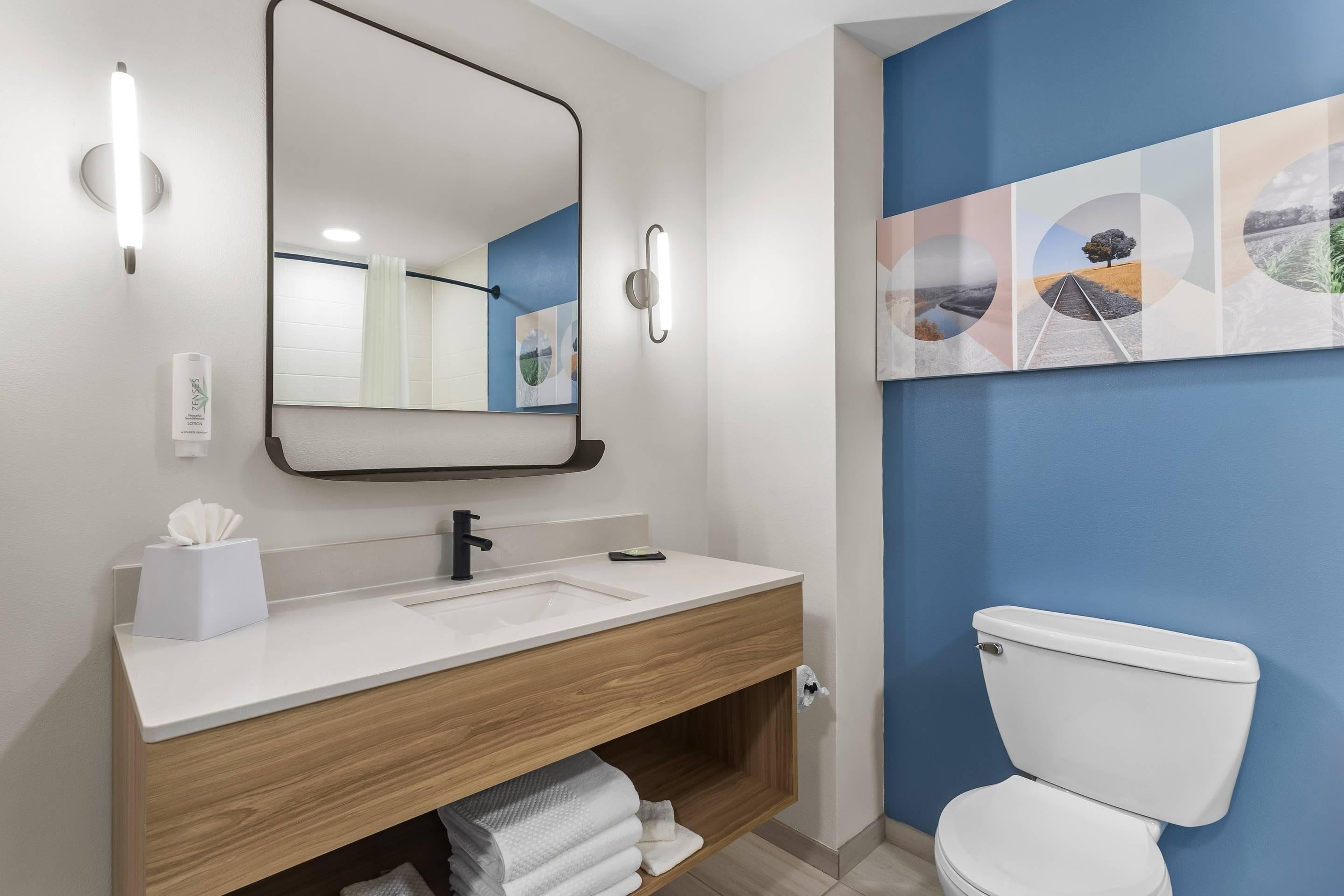 A modern bathroom with a white sink, wooden vanity, a large mirror, and a toilet.