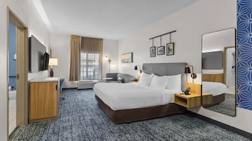 A hotel room with a bed, bedside tables, a desk, a chair, a TV, a window with curtains, and a mirror.