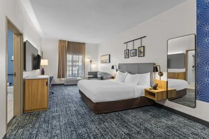 Habitación de hotel con cama, mesitas de noche, escritorio, silla, televisor, ventana con cortinas y espejo.