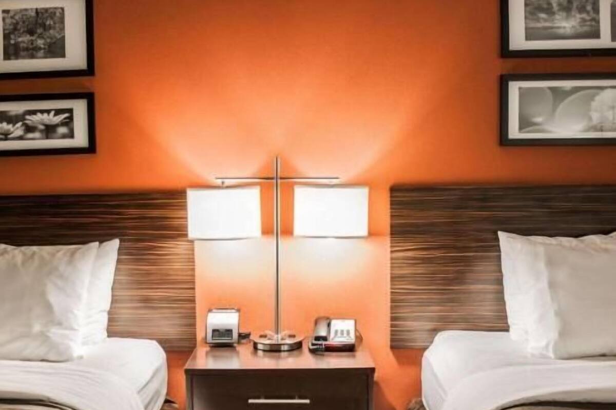 Habitación de hotel con dos camas, una mesita de noche con lámpara, teléfono y reloj.
