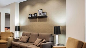 A modern living room with a sofa, two armchairs, and a coffee table. There are two floor lamps and a wall-mounted shelf with framed pictures.