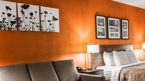 A hotel room with a sofa, a bed, a nightstand, and wall art.