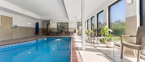 A swimming pool with a tiled edge, adjacent to a covered patio area with outdoor seating and potted plants.