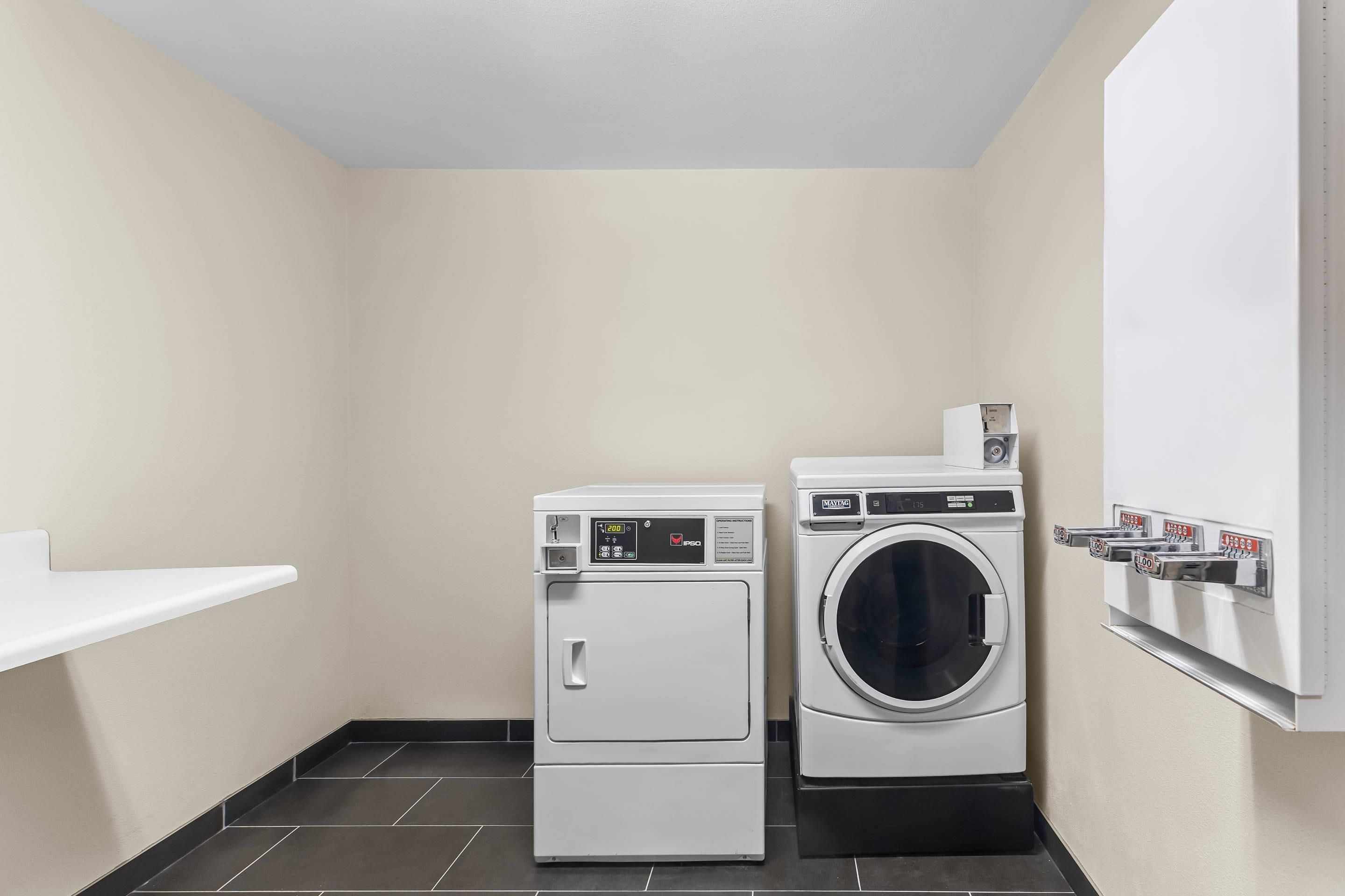 A compact laundry room with a front-loading washer and dryer, a small shelf, and a wall-mounted drying rack.
