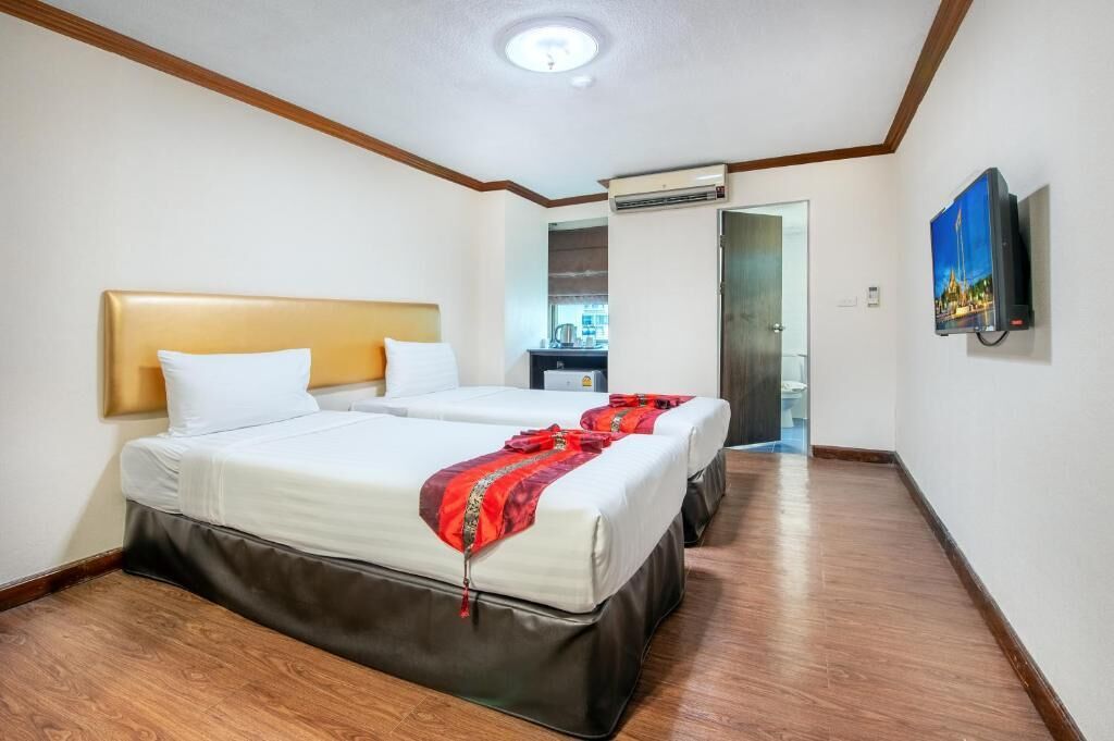 Habitación de hotel con dos camas, piso de madera, luz en el techo, aire acondicionado y televisor en la pared.