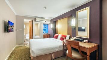 A hotel room with a large bed, a desk with a telephone, a mirror, and a television on the wall.