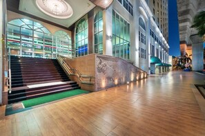 A spacious lobby with a grand staircase leading to upper floors, large windows, and a modern architectural design.