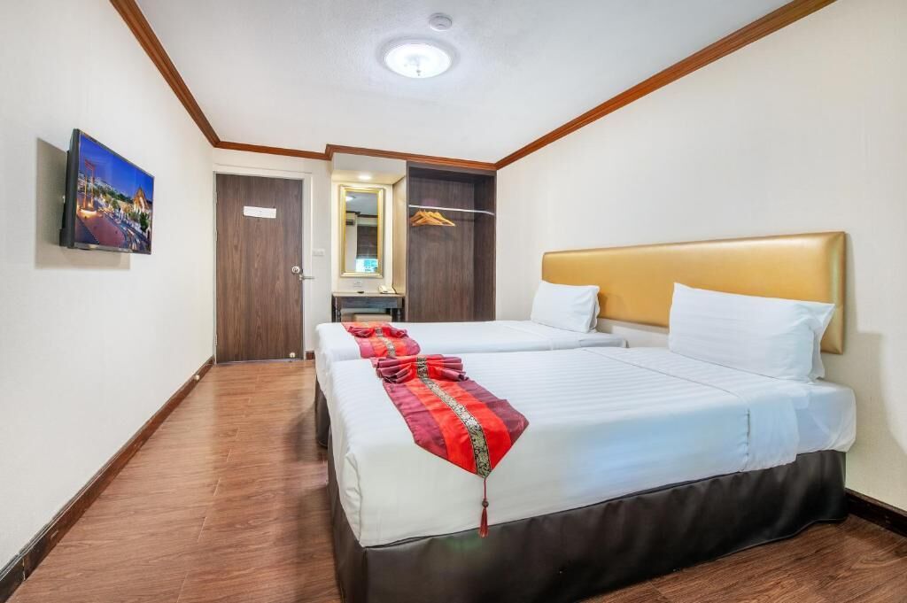 A hotel room with two beds, a wooden floor, a TV on the wall, and a mirror above the door.