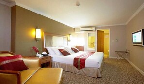 A hotel room with a bed, a desk, a chair, a TV, and an air conditioning unit.