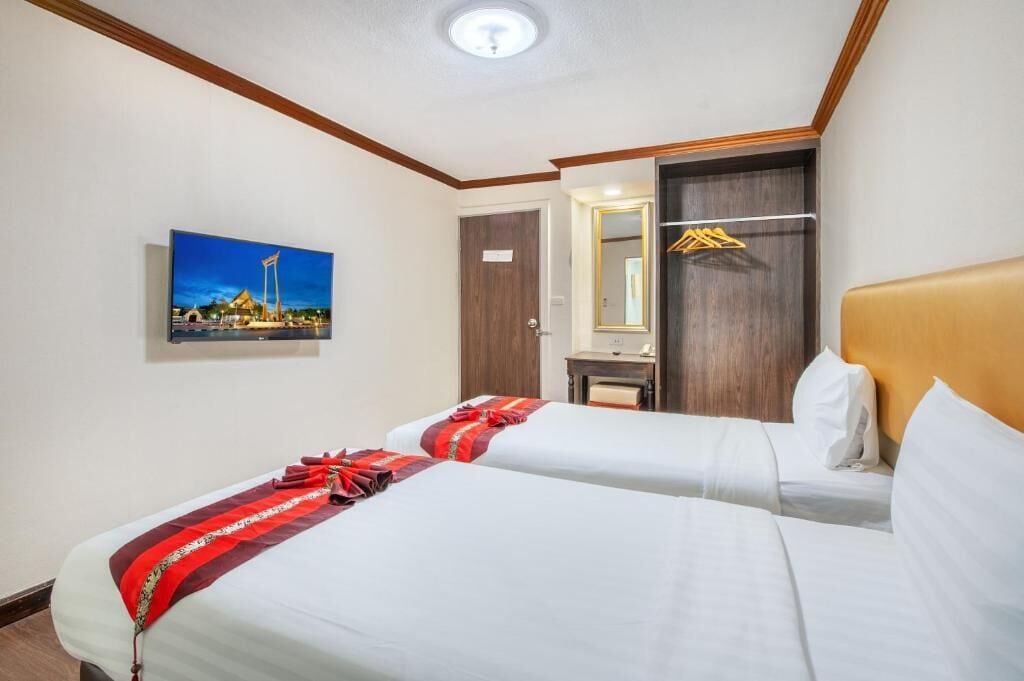Habitación de hotel con dos camas, cabecera de madera, espejo, perchero y un cuadro de un paisaje urbano.
