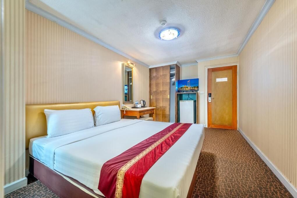 Una habitación de hotel con una cama grande, un escritorio con silla, un refrigerador pequeño y un televisor.