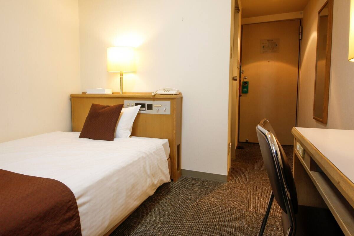 Ein Hotelzimmer mit einem Bett, einem Nachttisch mit Lampe, einem Telefon und einer Tür zu einem anderen Raum.