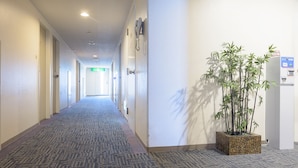Un pasillo de hotel con suelo alfombrado, puertas a la izquierda y una planta en maceta a la derecha.