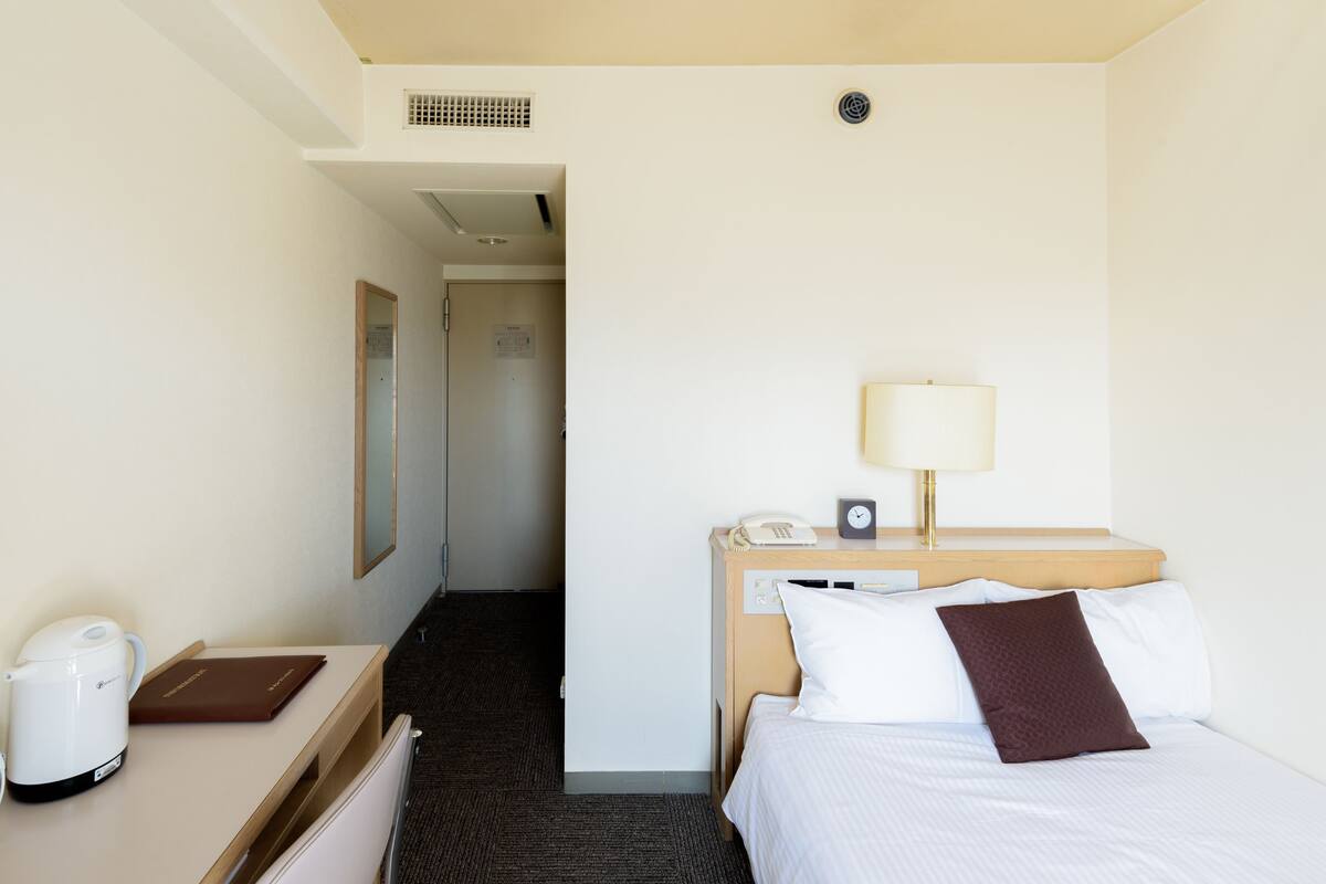 Ein Hotelzimmer mit Bett, Nachttisch, Lampe und Blick auf den Flur.