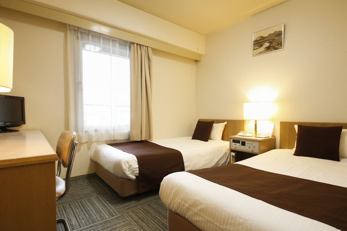 Ein Hotelzimmer mit zwei Betten, einem Schreibtisch, einem Stuhl, einer Lampe und einem Bild an der Wand.