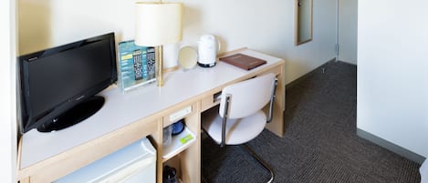 A hotel room with a desk, a television, a lamp, a coffee maker, a book, and a mirror.
