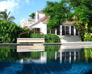 A clear swimming pool with a reflection of a white building and lush greenery.