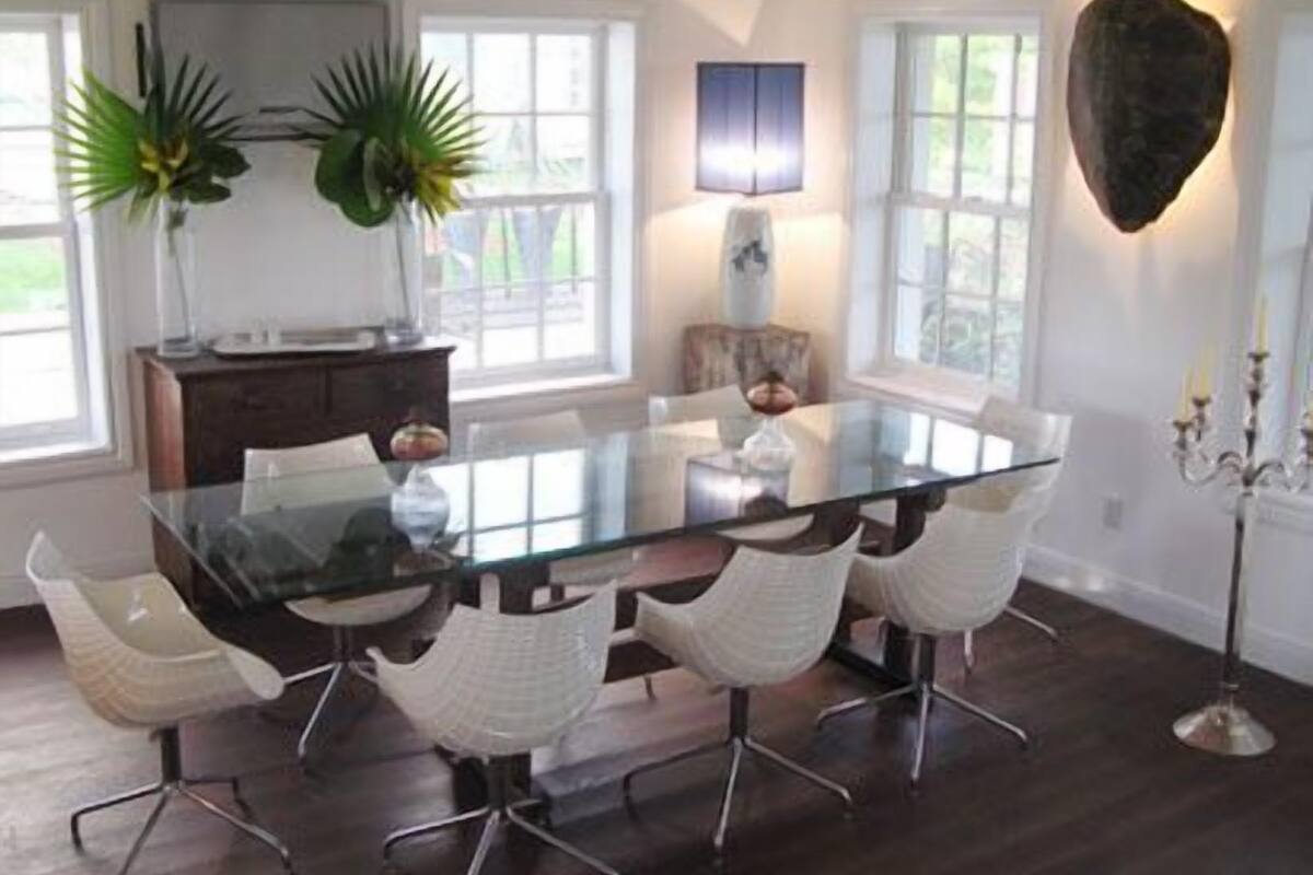 A dining area with a glass table surrounded by white chairs, a dark wooden floor, and a chandelier.