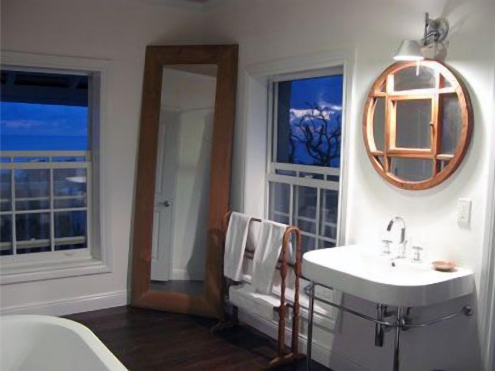 Un baño con un lavabo blanco, un espejo con marco de madera y vistas al exterior a través de una ventana.