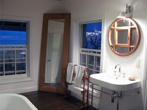 A bathroom with a white sink, a mirror with a wooden frame, and a view of the outdoors through a window.