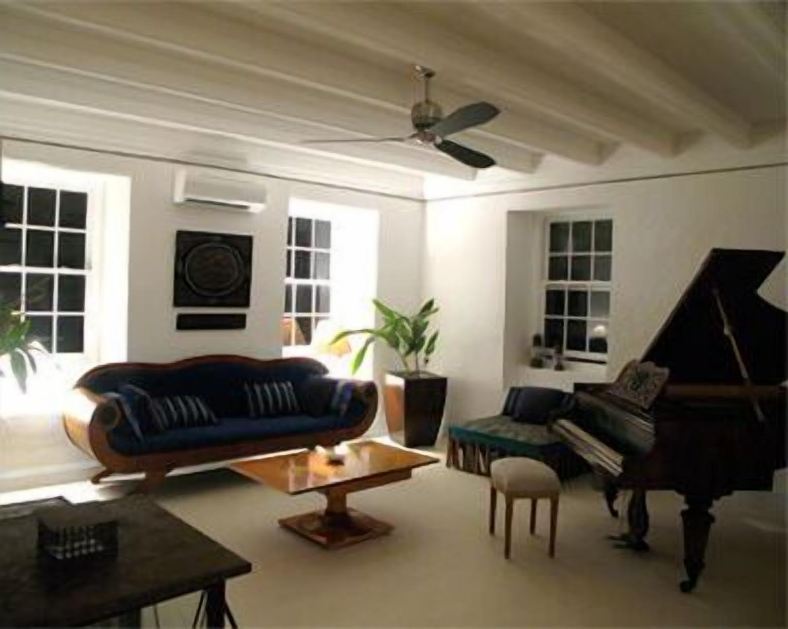 A living room with a blue sofa, a small table, a piano, and a ceiling fan.