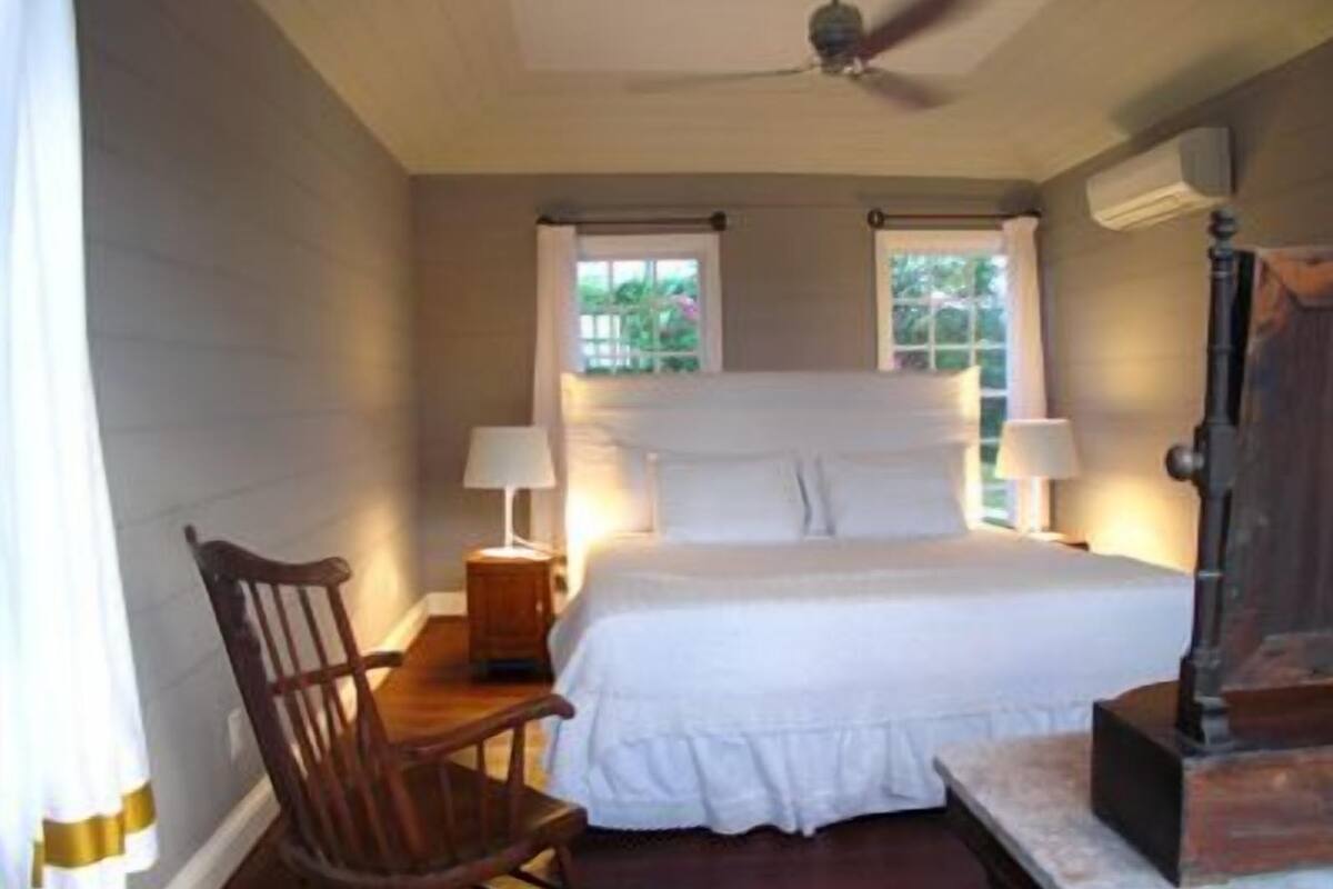 A bedroom with a large bed, two bedside lamps, a wooden chair, a small table, and a ceiling fan.