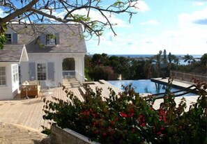 A house with a large swimming pool, a covered deck, and a view of the ocean.