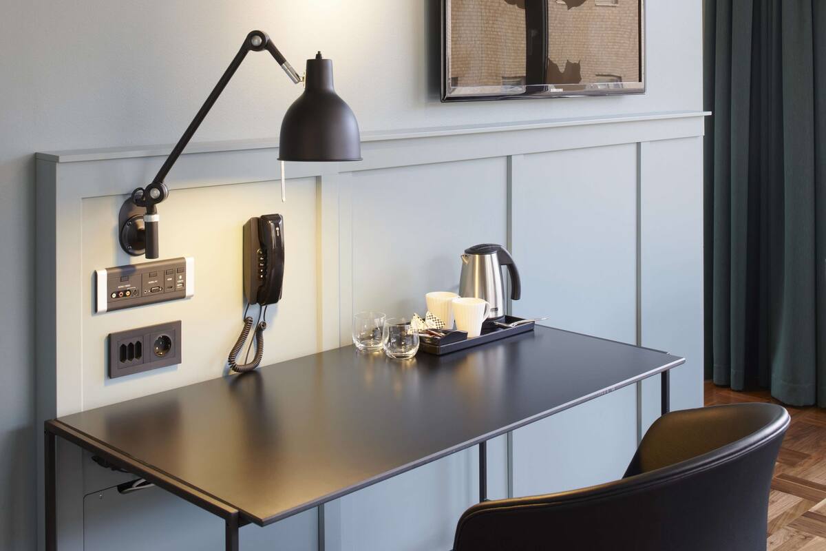Habitación de hotel moderna con escritorio, teléfono, cafetera e imagen enmarcada en la pared.