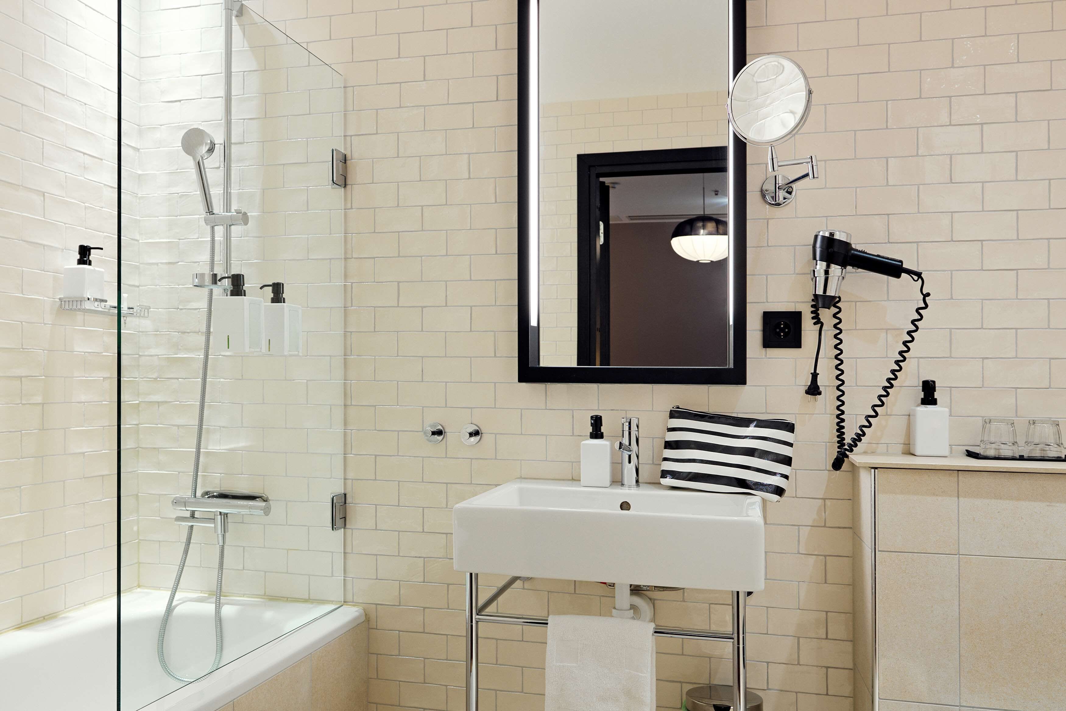 Un baño moderno con ducha de vidrio, lavamanos blanco con espejo arriba y secador de pelo en la pared.