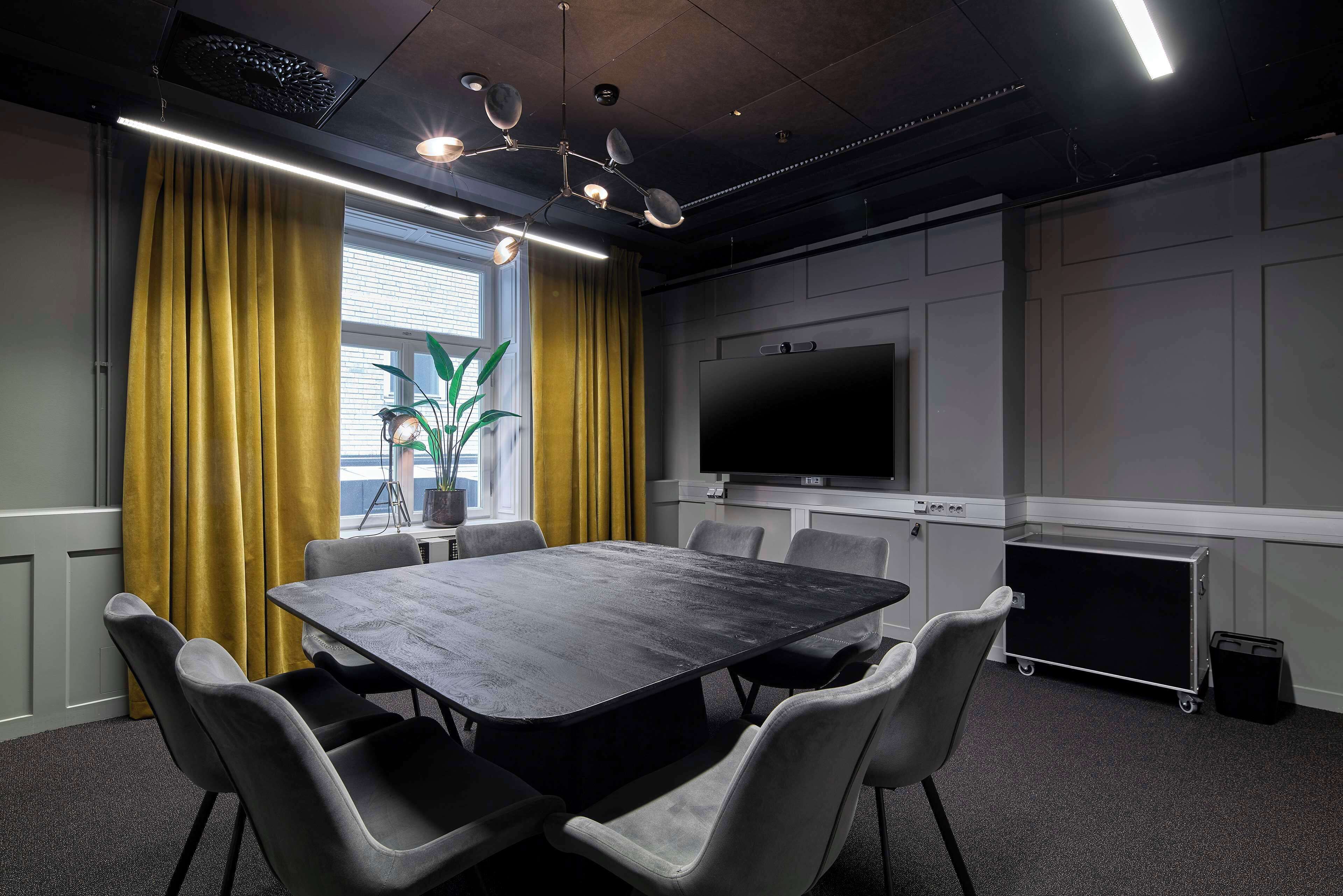 Un salón de conferencias con una mesa grande, seis sillas, un televisor y un carrito.