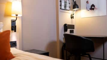 Une chambre d’hôtel équipée d’un lit, d’un bureau, d’une chaise, d’une lampe et d’un téléphone fixé au mur.