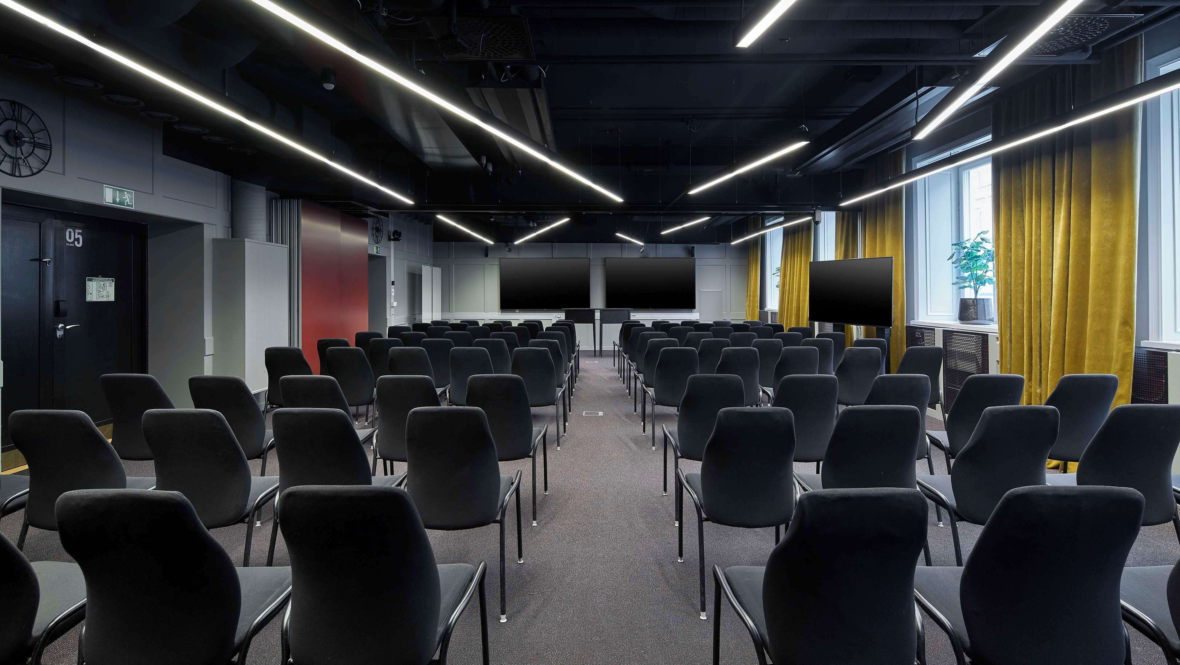 A conference room with rows of chairs, a clock, and a door labeled "05".