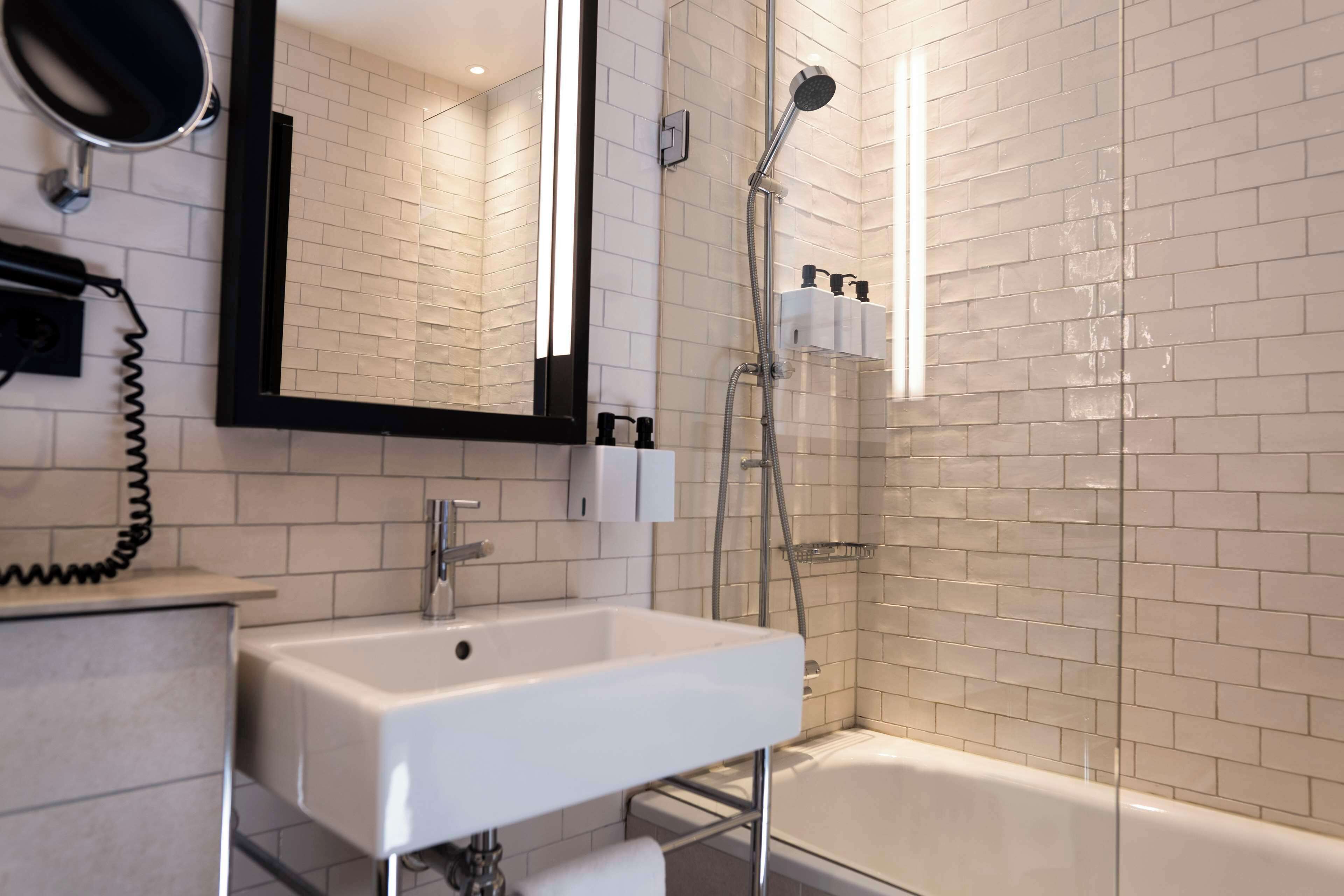 Ein modernes Badezimmer mit einem weißen Waschbecken, einem Spiegel, einer Duschbrause und einer Badewanne.
