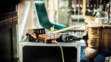 A guitar, headphones, and a suitcase on a table in a room with a blue chair and wooden furniture.