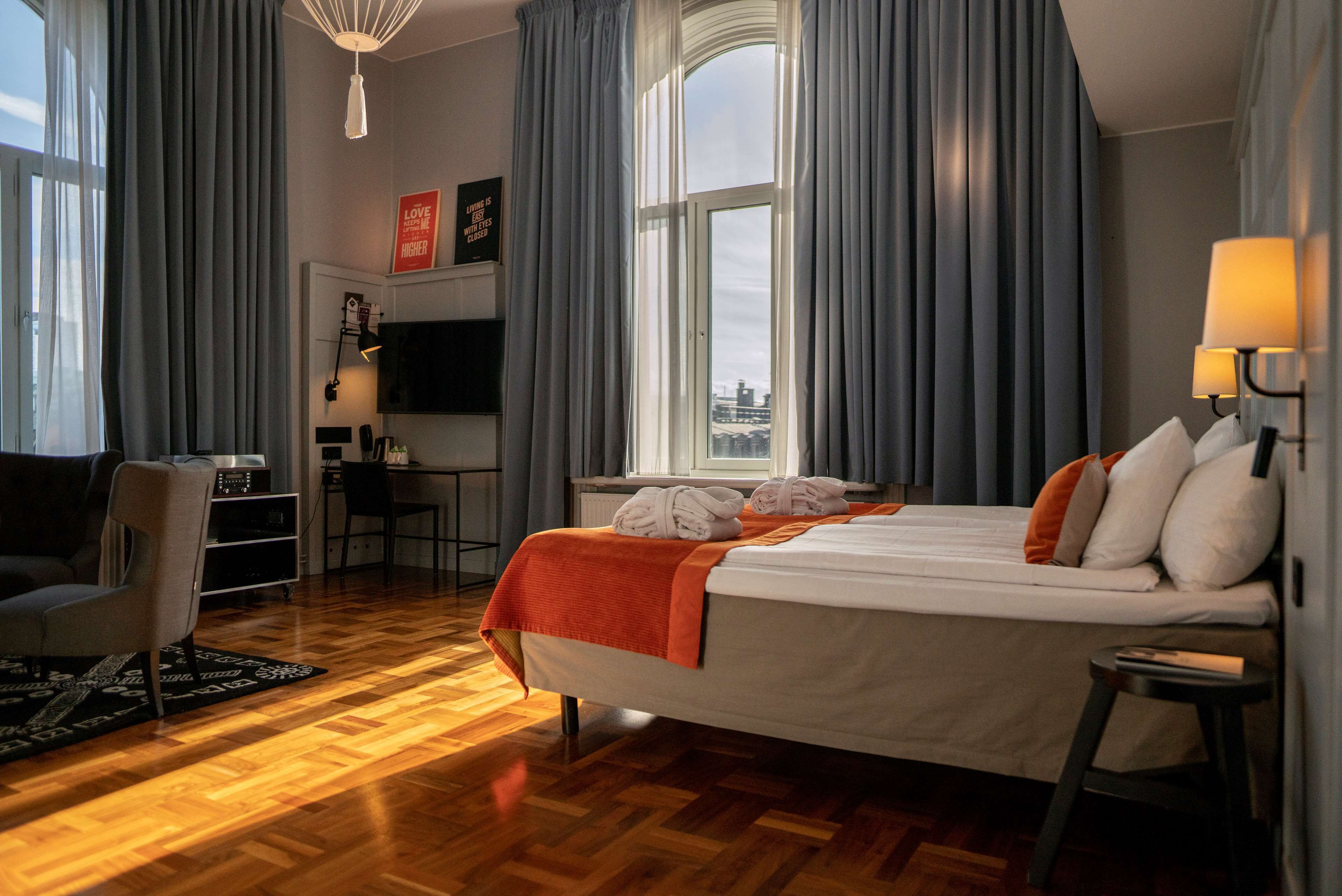 A hotel room with a large bed, a desk with a chair, a TV, and a city view.
