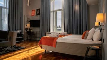 Habitación de hotel con una cama grande, un escritorio con silla, televisión y vista a la ciudad.