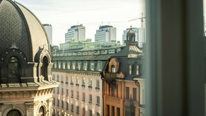 Un edificio hist órico con una cúpula destacada y arquitectura clásica, visto desde una ventana que da a un paisaje urbano con edificios modernos.