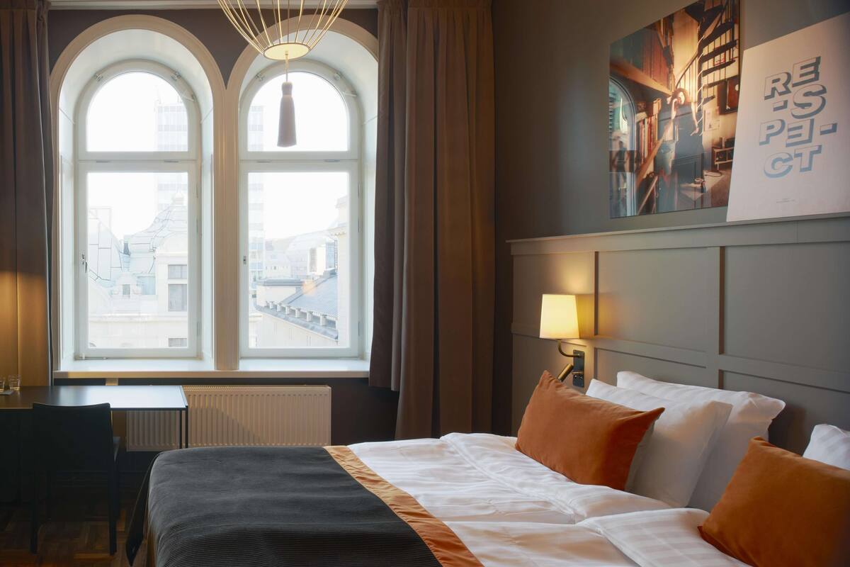 Habitación de hotel con una cama grande, un escritorio y una ventana con vistas a edificios.