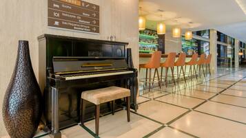 Um piano perto de uma parede com sinalização, área de bar com cadeiras e vista para o exterior através de grandes janelas.