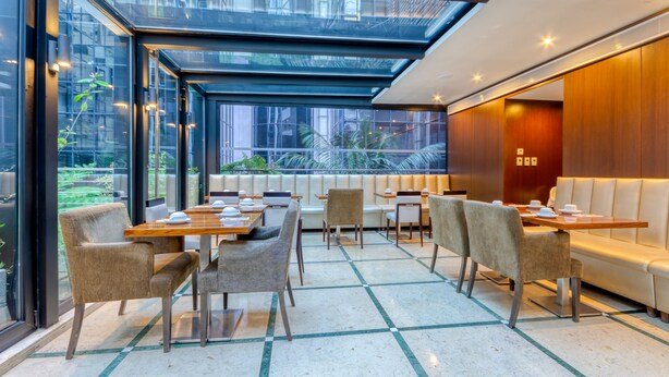 Un comedor moderno con paredes de vidrio, mesas, sillas y un banco de madera.
