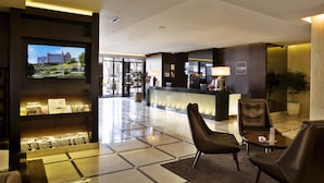 Vestíbulo de hotel con mostrador de recepción, zona de estar y un televisor que muestra una vista panorámica.