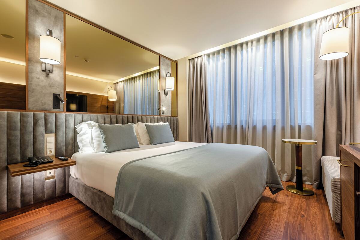 Ein Hotelzimmer mit einem großen Bett, Nachttischen, einem Spiegel und einem Schreibtisch mit Lampe.