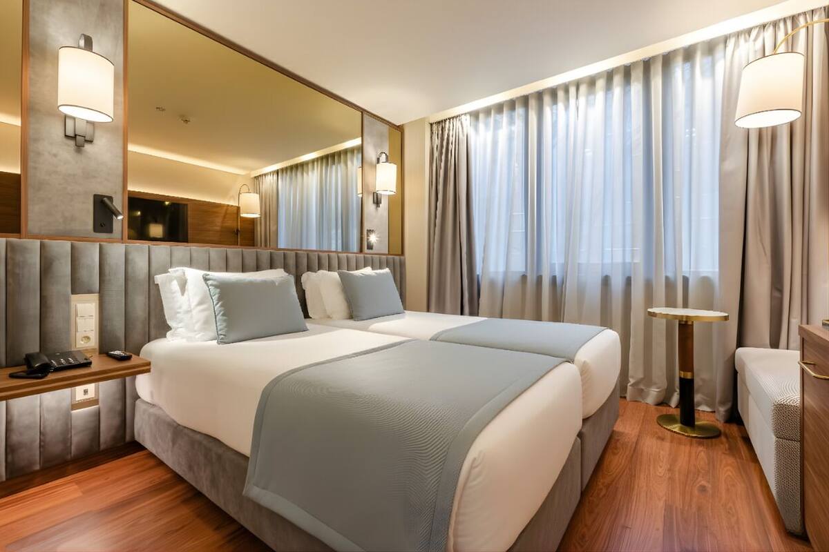 Ein Hotelzimmer mit einem großen Bett, Nachttischen, einem Schreibtisch, einem Sessel, einem runden Tisch und einem großen Spiegel.