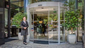 Entrada de hotel con puerta giratoria, puertas de cristal y plantas en macetas.
