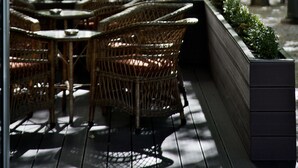 Un café al aire libre con mobiliario de mimbre y una jardinera.