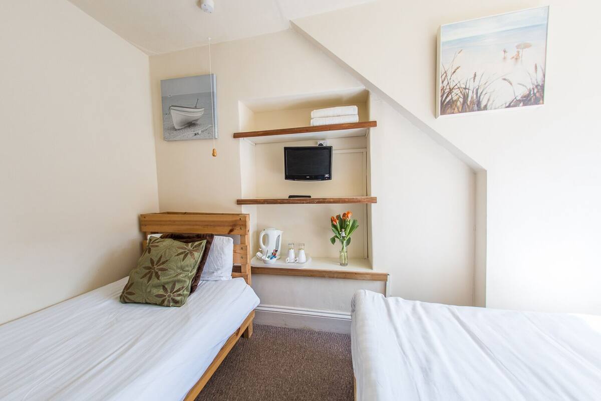 A hotel room with two single beds, a TV, a small shelf with toiletries, and a painting on the wall.